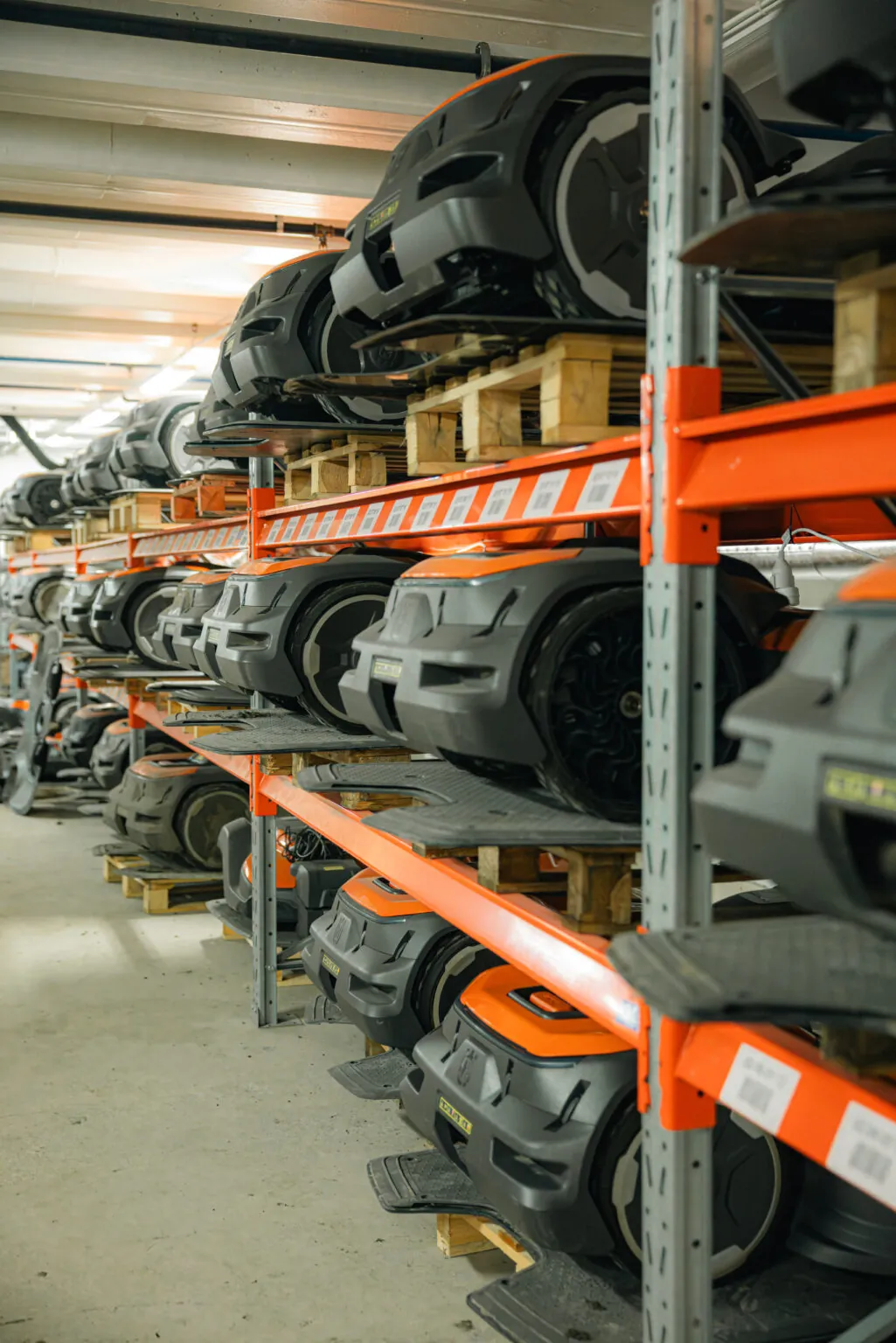 Robotgräsklippare från Husqvarna och andra märken lagrade på orange pallställ i verkstadslokal