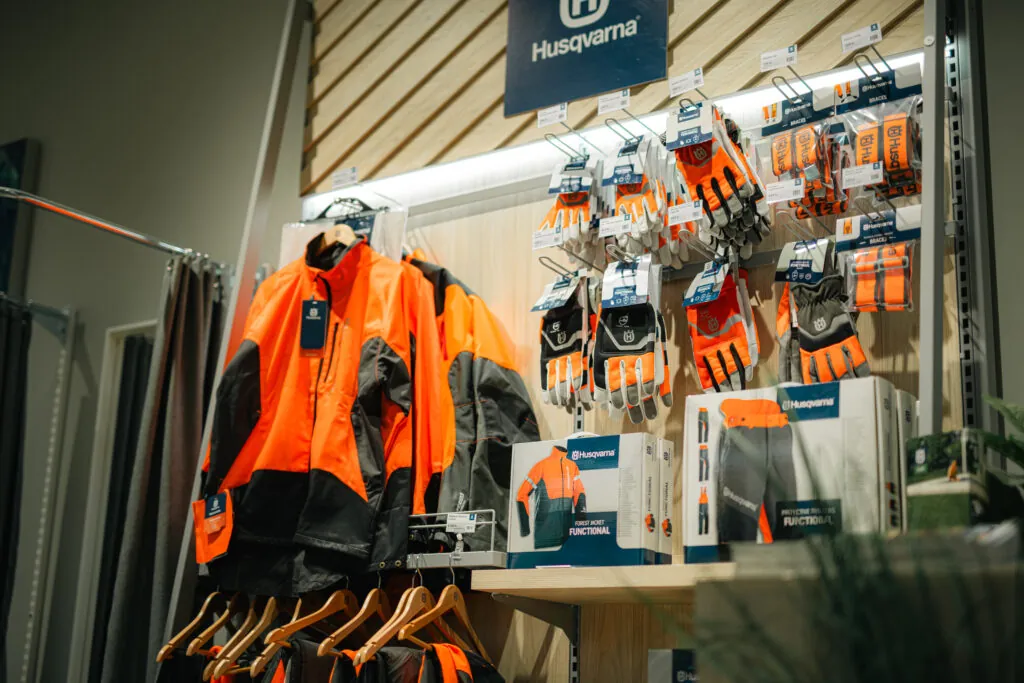 Husqvarna skyddsutrustning - orangea skogsjackor och skyddshandskar för motorsågsarbete i butikshylla