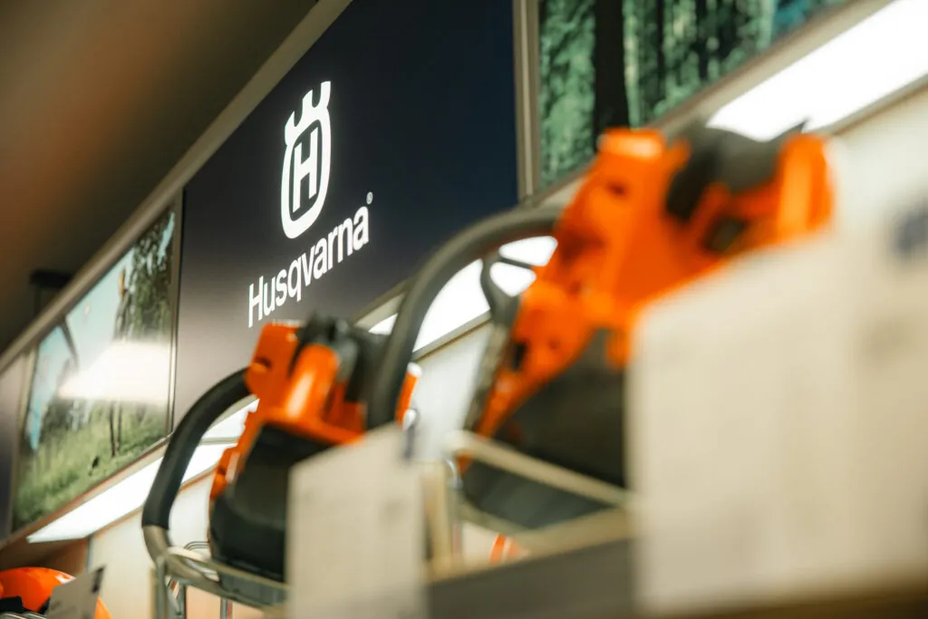 Husqvarna motorsågar med orange färg på hyllor i butik med Husqvarna-skylt på väggen