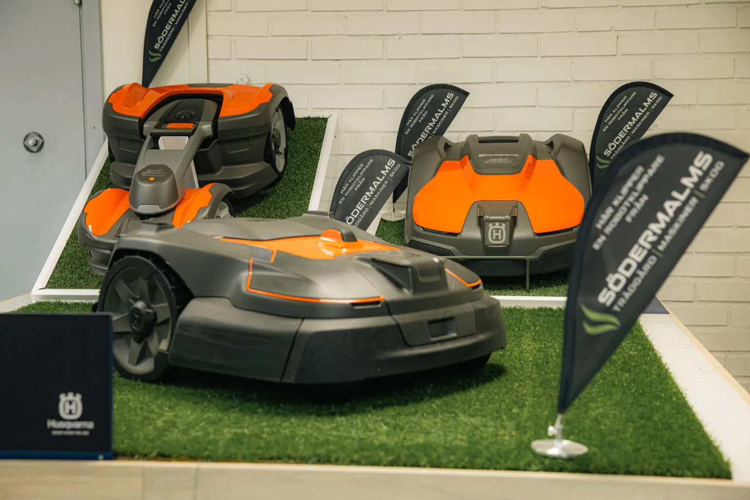 Husqvarna robotgräsklippare i grått och orange på konstgräs med informationsskyltar i butiksmiljö