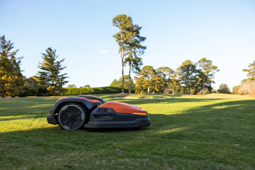Robotgräsklippare arbetar på golfbana med välklippt gräs och träd i bakgrunden